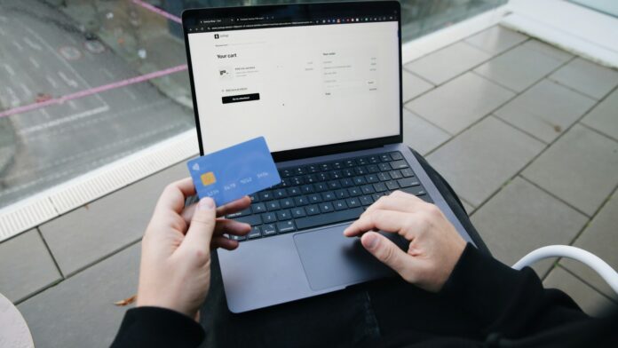 A person holding a credit card while paying on a laptop